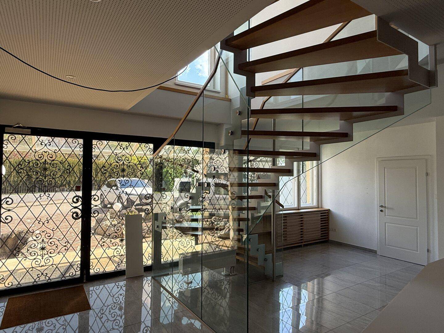 Moderner Eingangsbereich mit einer eleganten Wendeltreppe aus Holz und Glas sowie glänzenden Fliesen.