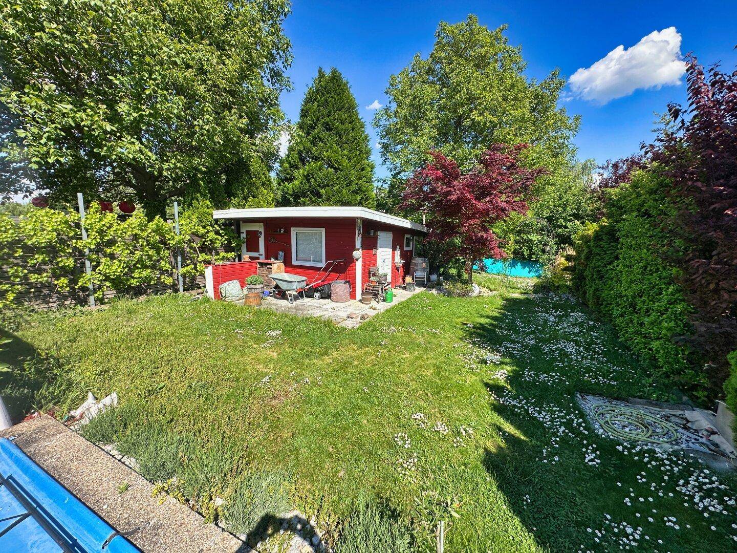 Gepflegter Garten mit Rasenfläche, Bäumen und einem roten Gartenhaus.