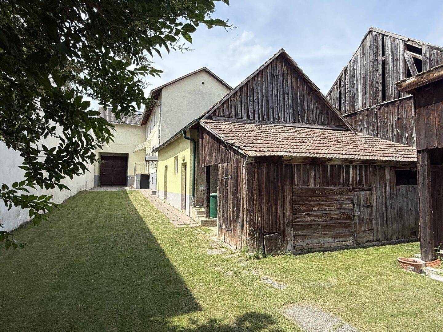 Weitläufiger Gartenbereich mit Rasen, Hauptgebäude und mehreren rustikalen Nebengebäuden aus Holz.