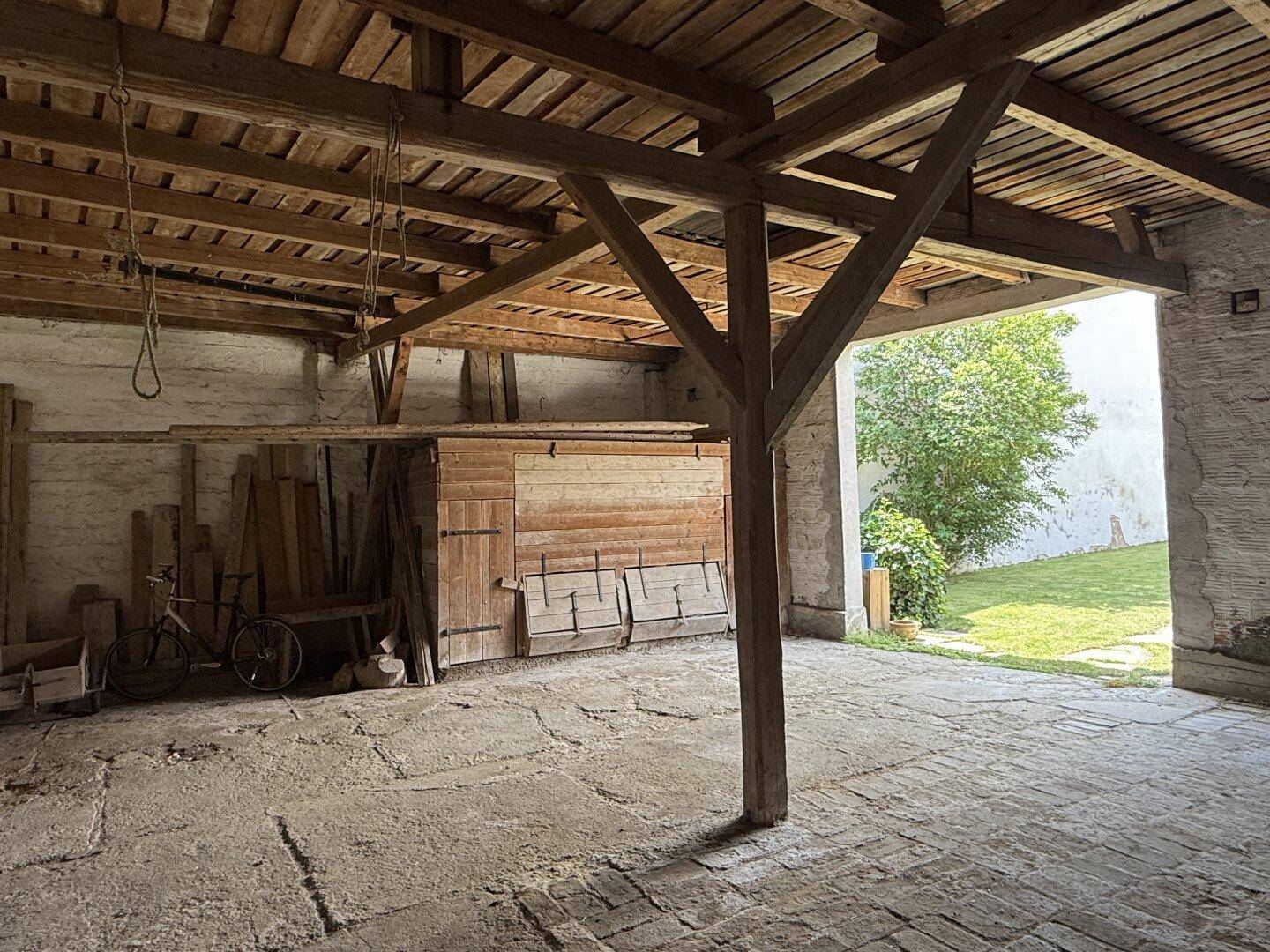 Heller Innenraum eines Nebengebäudes mit Holzbalken und Blick auf den grünen Gartenbereich.