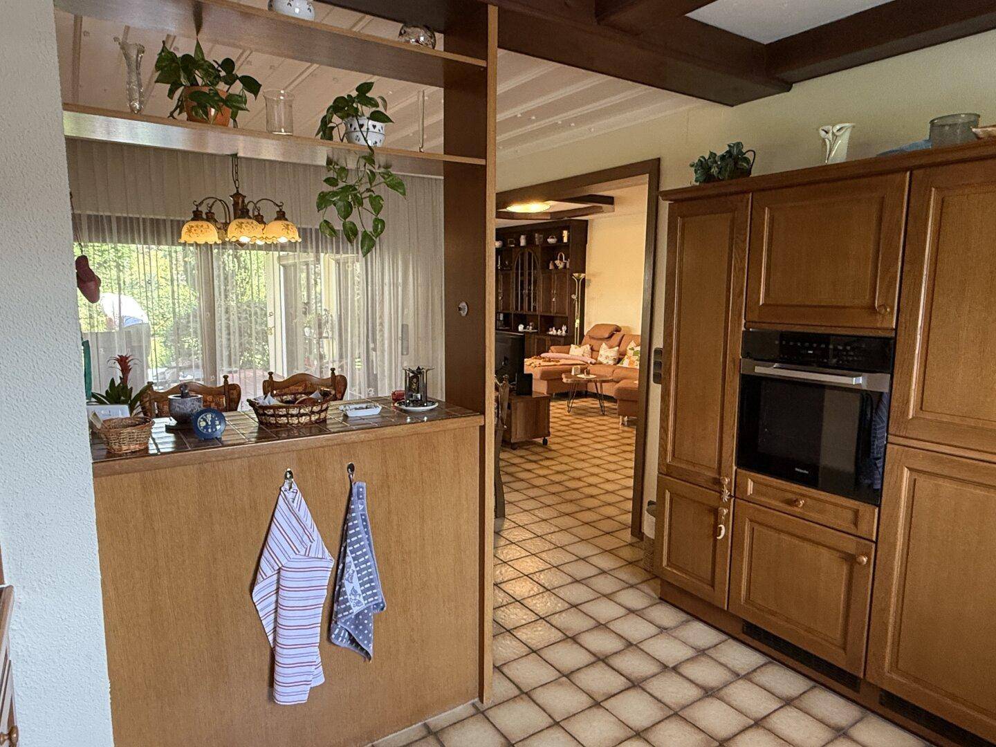 Küchenbereich mit Durchgang zum Wohnzimmer, ausgestattet mit Holzmöbeln und Einbauofen.