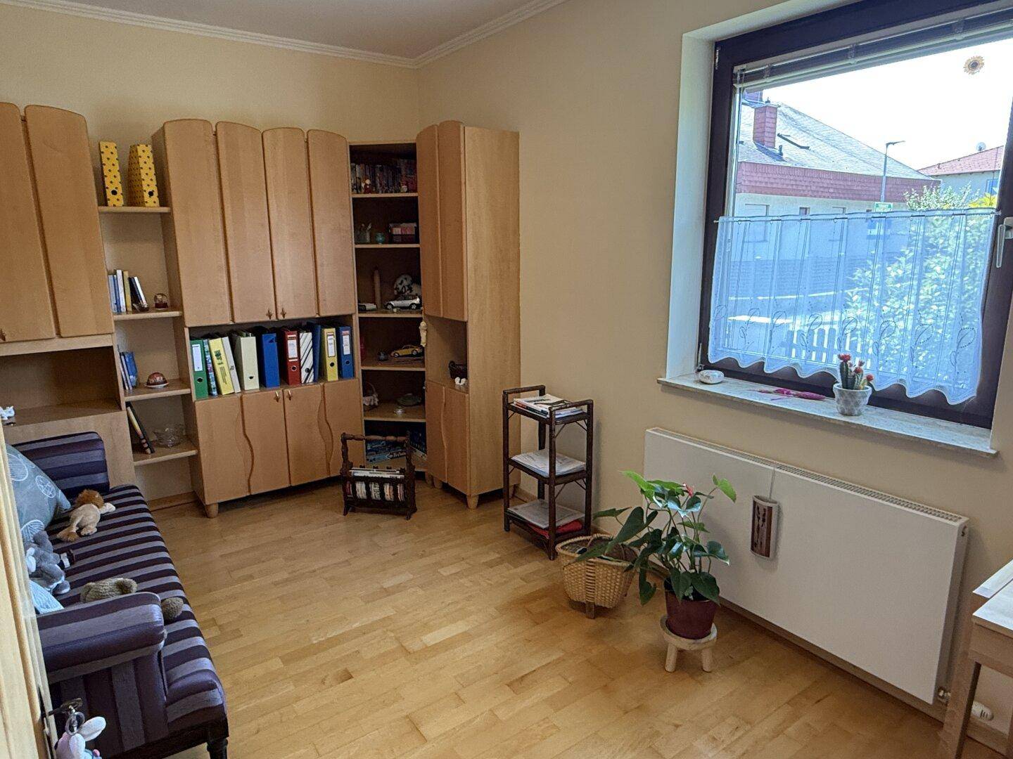 Helles Arbeitszimmer mit Holzschränken, Parkettboden und Fensterblick ins Grüne.