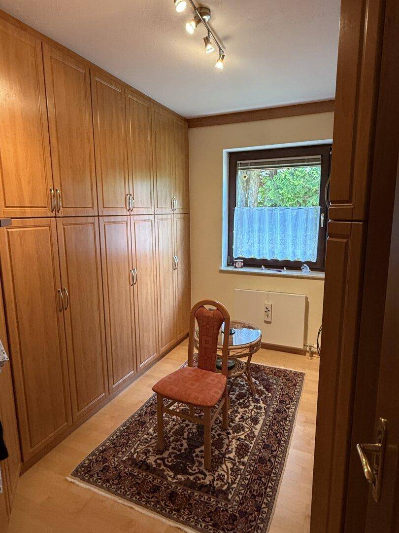 Schlafzimmer mit großen Holzschränken, Parkettboden und Fenster mit Vorhängen.