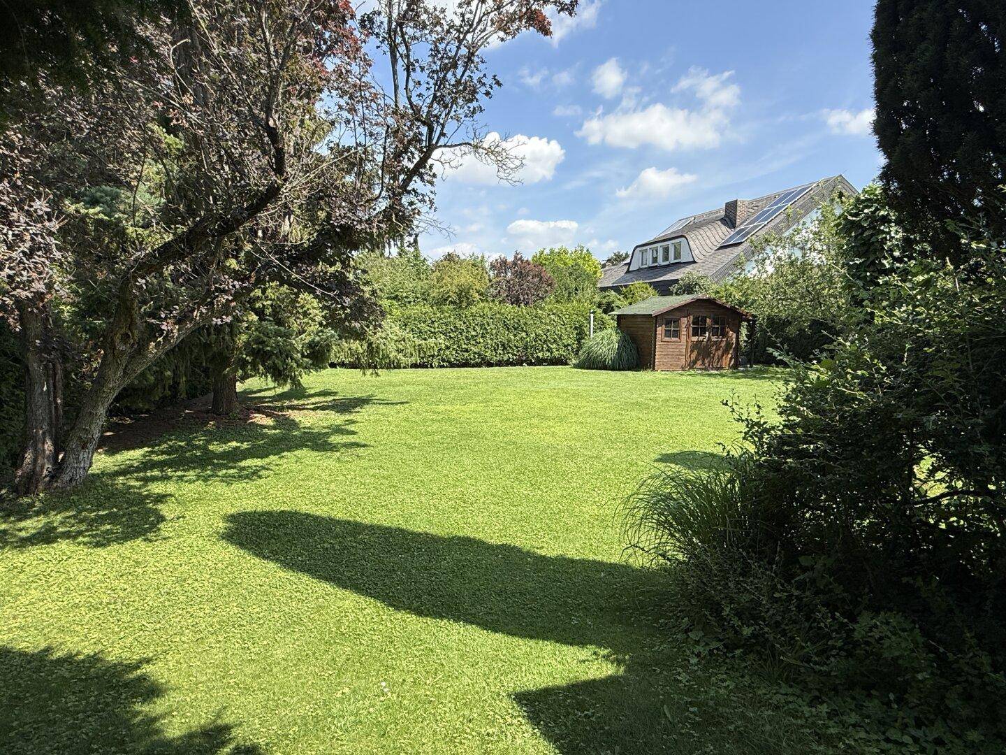 Großer, gepflegter Garten mit Rasenfläche, Bäumen und Gartenhaus im Hintergrund.
