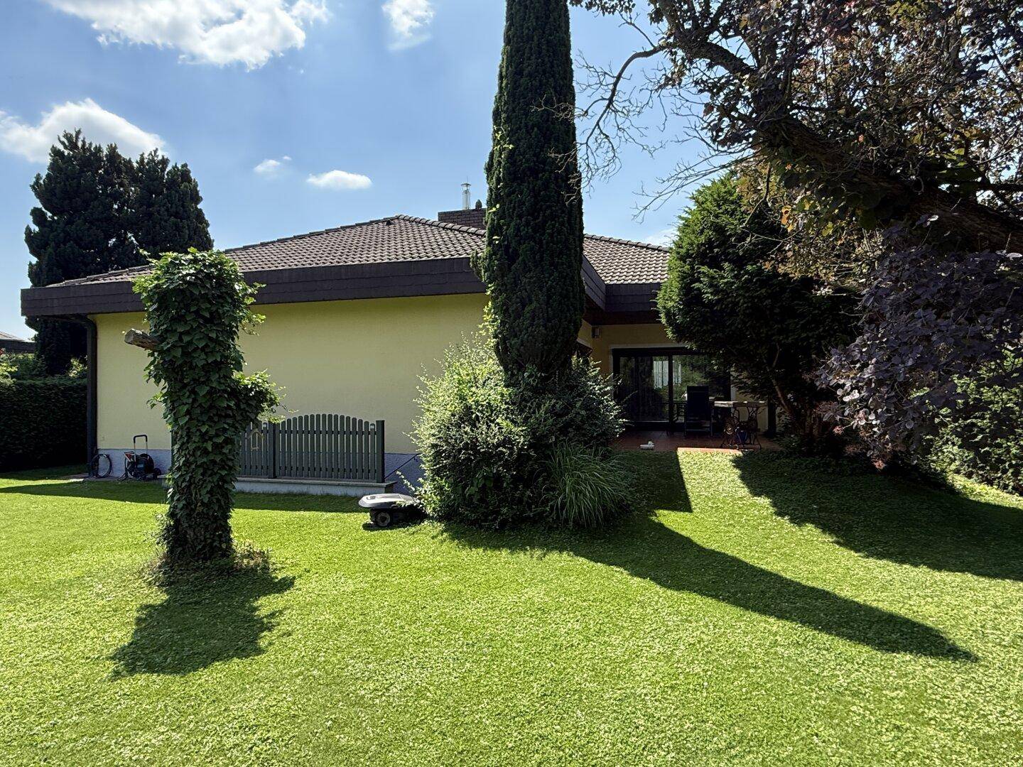 Gepflegter Garten mit Rasen, hohen Bäumen und Blick auf die Rückseite des Hauses.