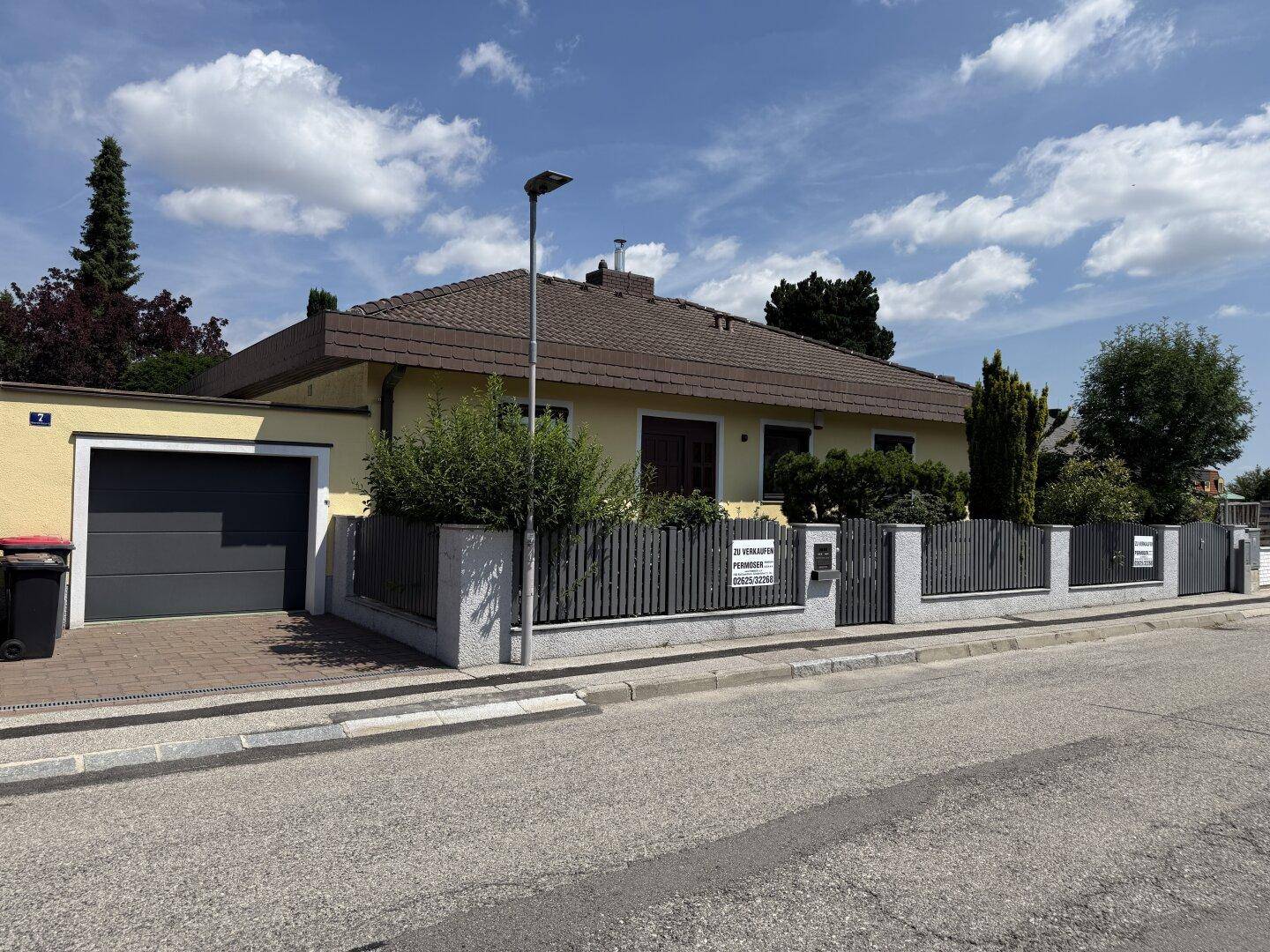 Ansicht des Einfamilienhauses von der Straße mit Garage, Vorgarten und Zaun.