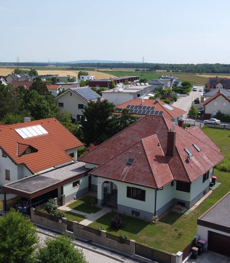 Luftaufnahme des Einfamilienhauses mit umliegender Nachbarschaft und Feldern im Hintergrund.