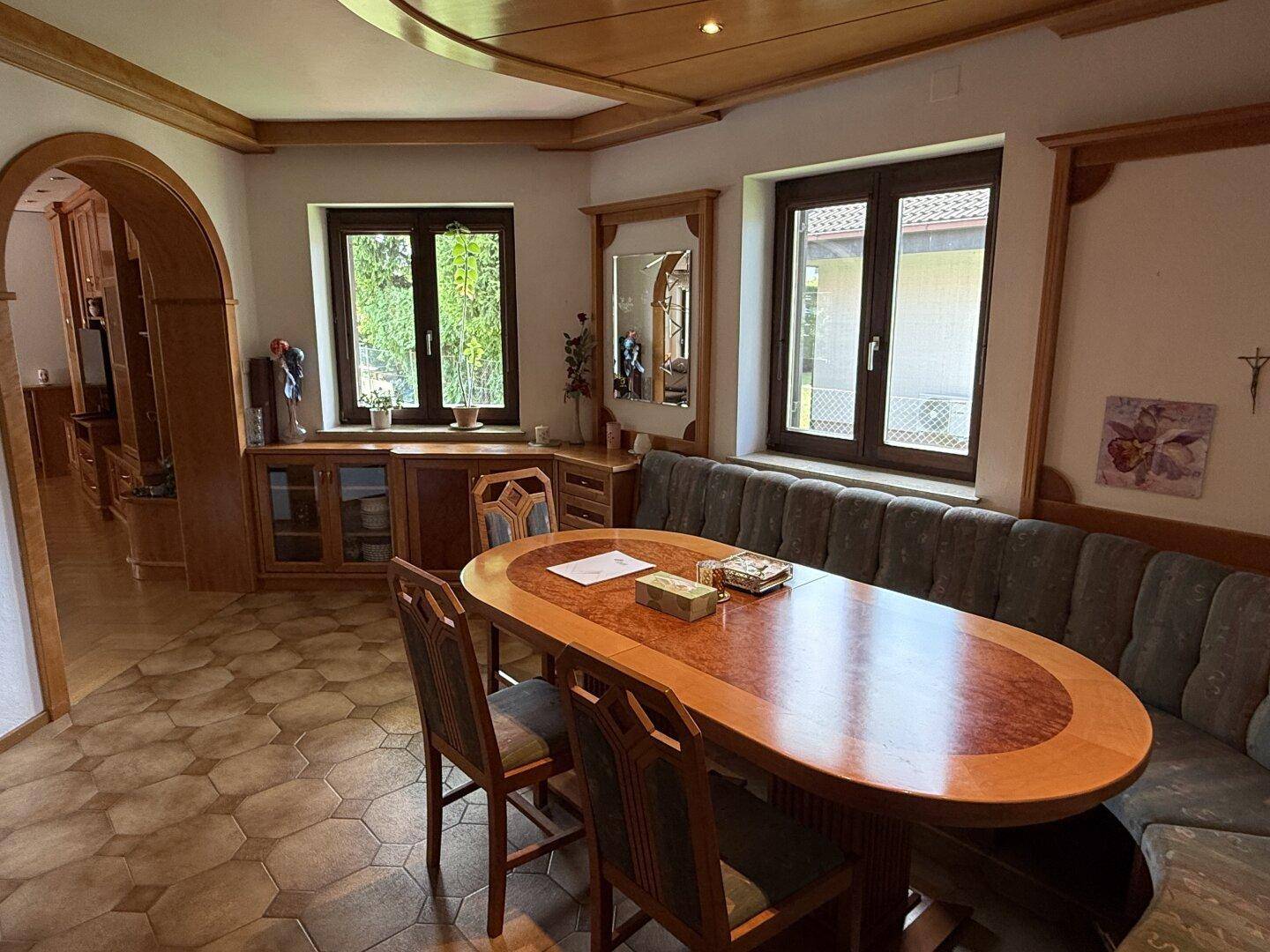 Gemütlicher Essbereich mit Holztisch, Eckbank und Blick in den Garten durch die Fenster.