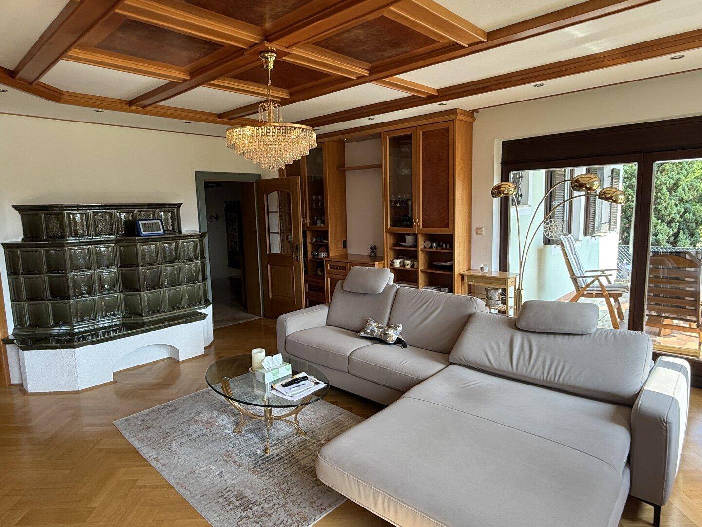 Helles Wohnzimmer mit Kachelofen, bequemer Couch und Zugang zum Balkon.