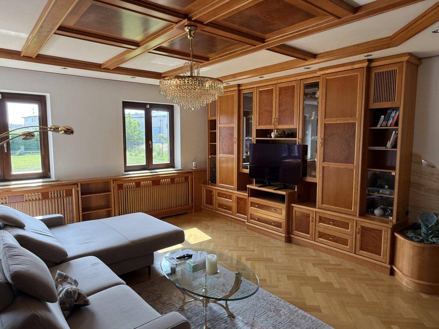 Geräumiges Wohnzimmer mit großer Holzschrankwand, Parkettboden und Fenstern.