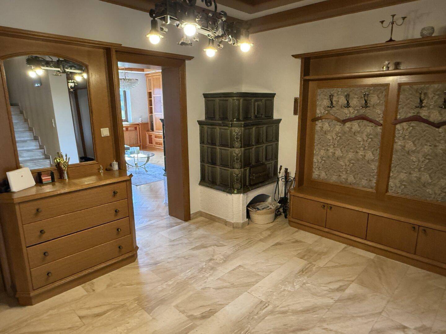 Eingangsbereich mit traditionellem Kachelofen, Holzkommode und Marmorboden.