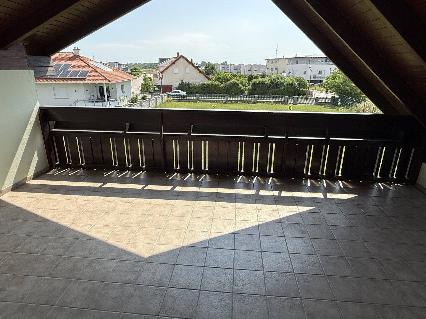 Geräumiger Balkon mit Fliesenboden, Holzgeländer und weitem Blick über die Nachbarschaft.