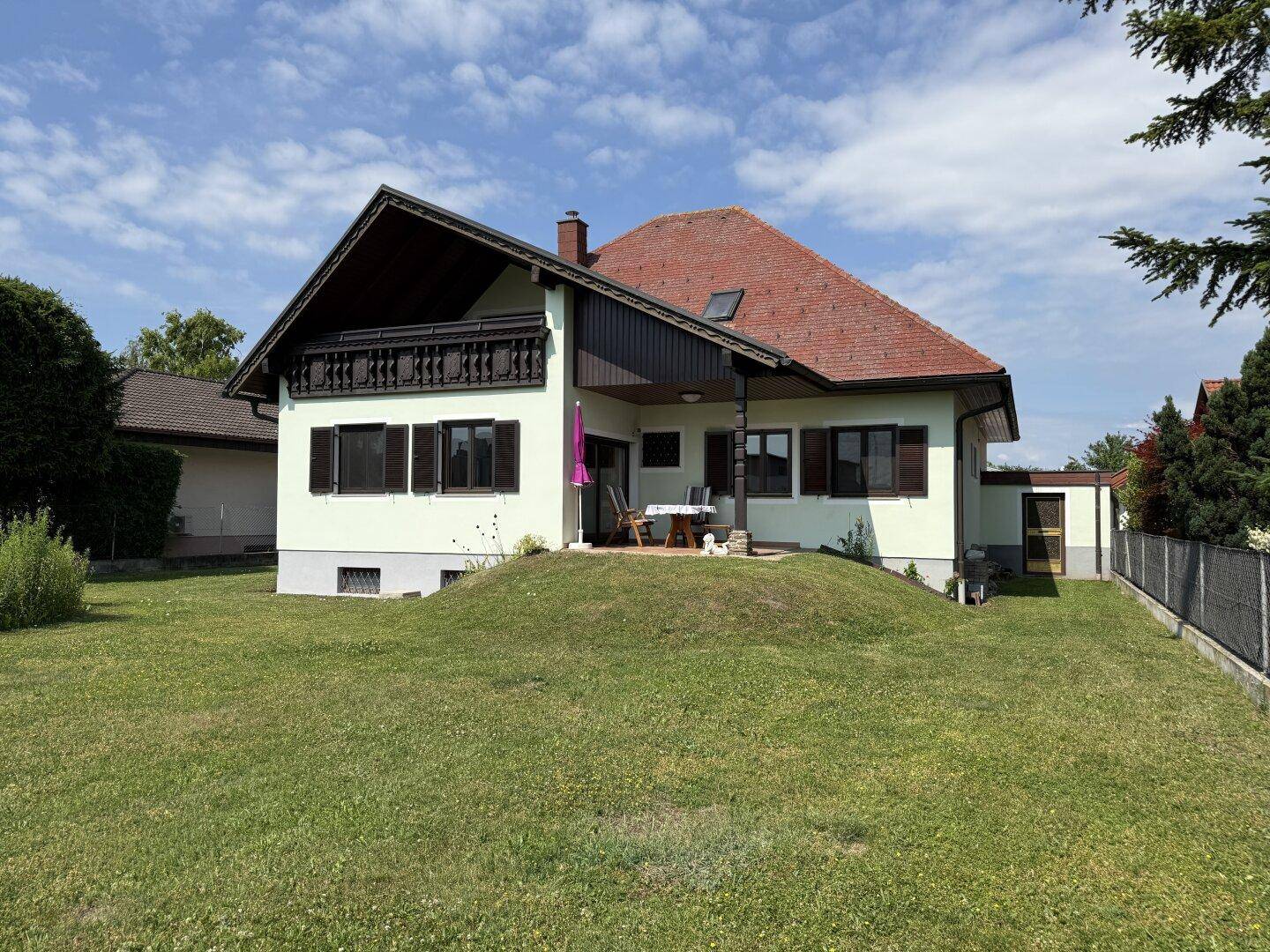 Rückseite des Hauses mit Terrasse, großem Rasen und Gartenmöbeln.