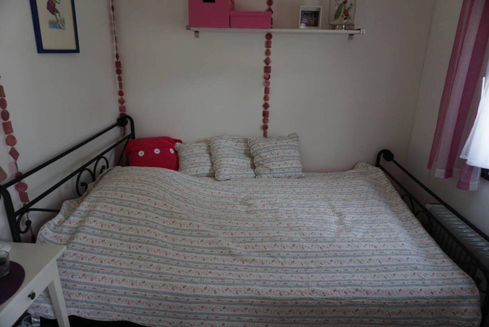 Schlafzimmer mit Metallbett, gemusterter Bettdecke und farbenfroher Dekoration.