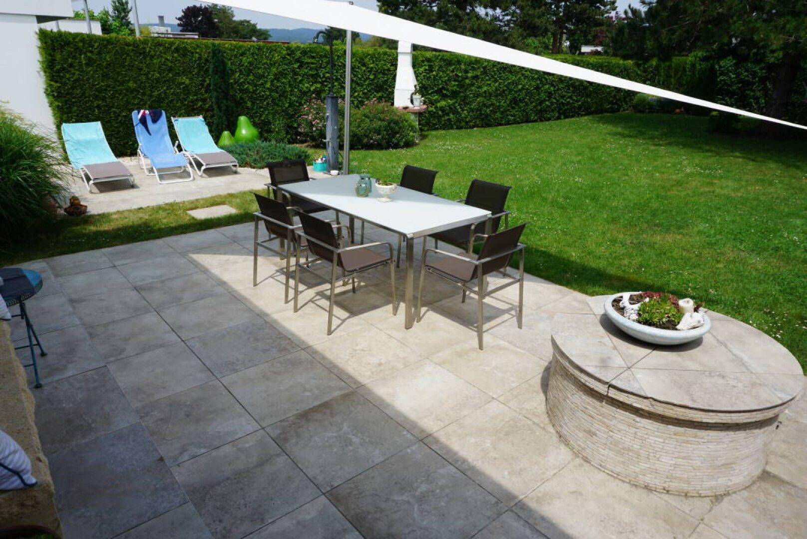 Große gepflasterte Terrasse mit Esstisch und Liegestühlen, angrenzend an den Rasen.