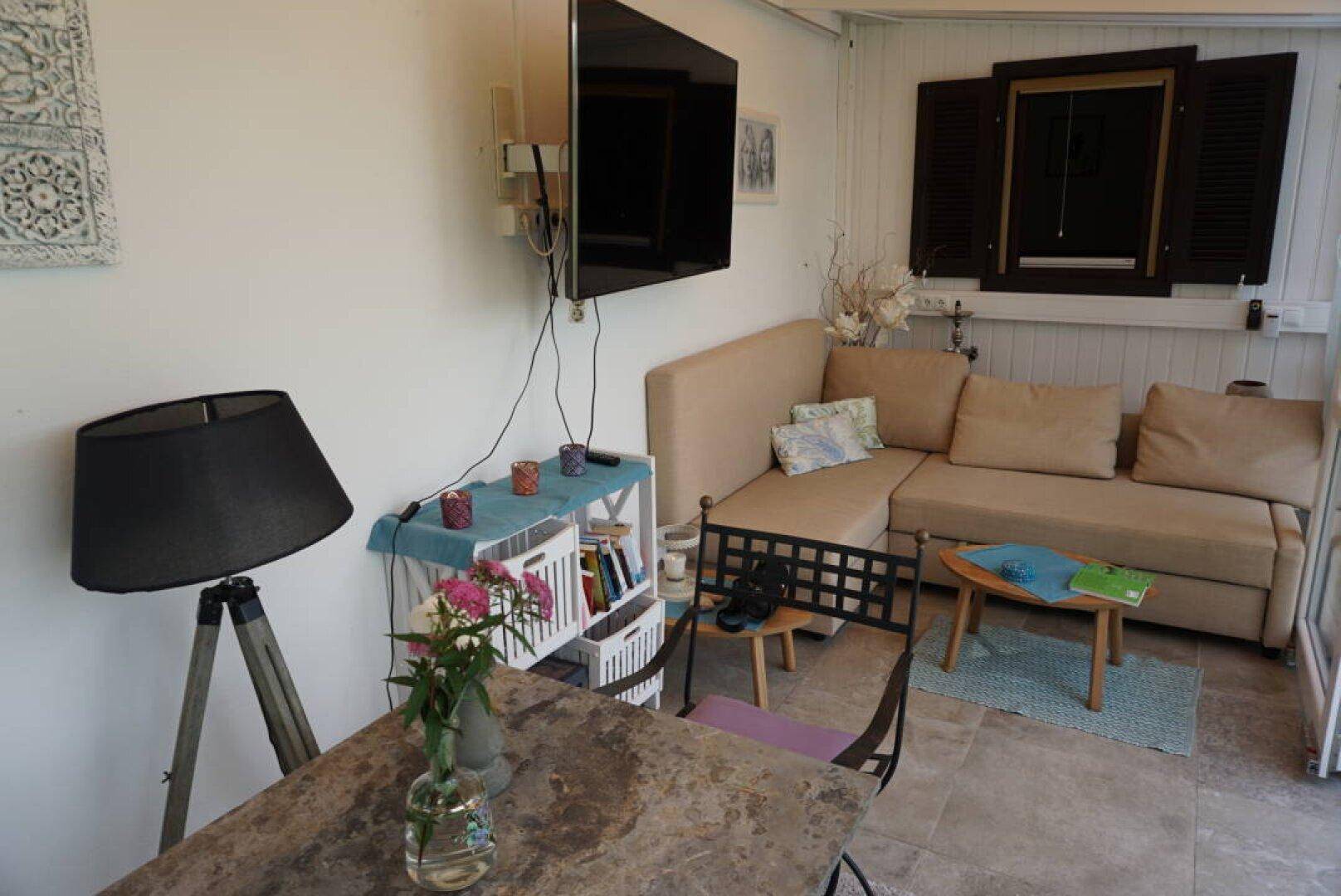 Gemütlicher Wintergarten mit Sofa, Fernseher und kleinem Tisch, ideal zum Entspannen.