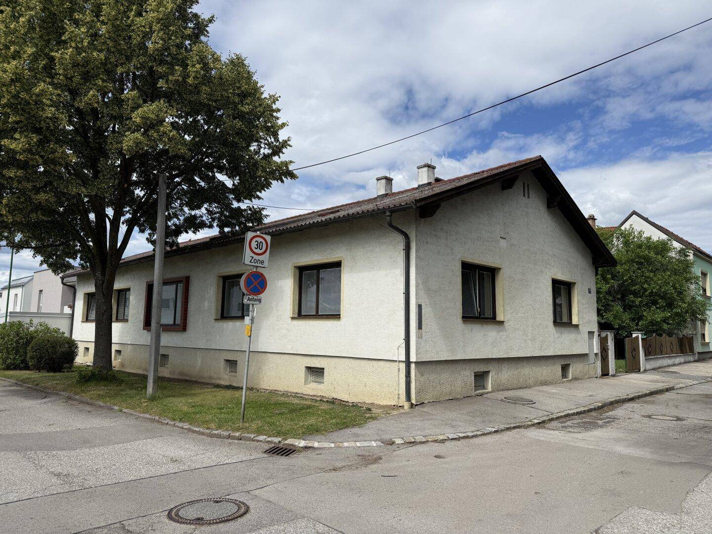 Eckansicht des Hauses mit gepflegter Fassade, umgeben von Bäumen und einer ruhigen Straße.