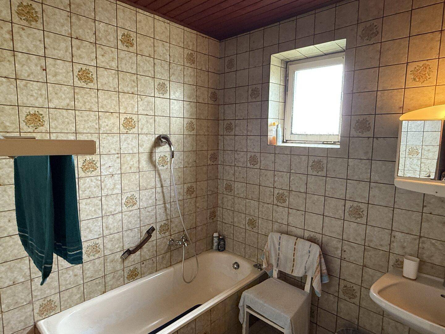 Badezimmer mit gemusterten Wandfliesen, Badewanne und kleinem Fenster für Tageslicht.