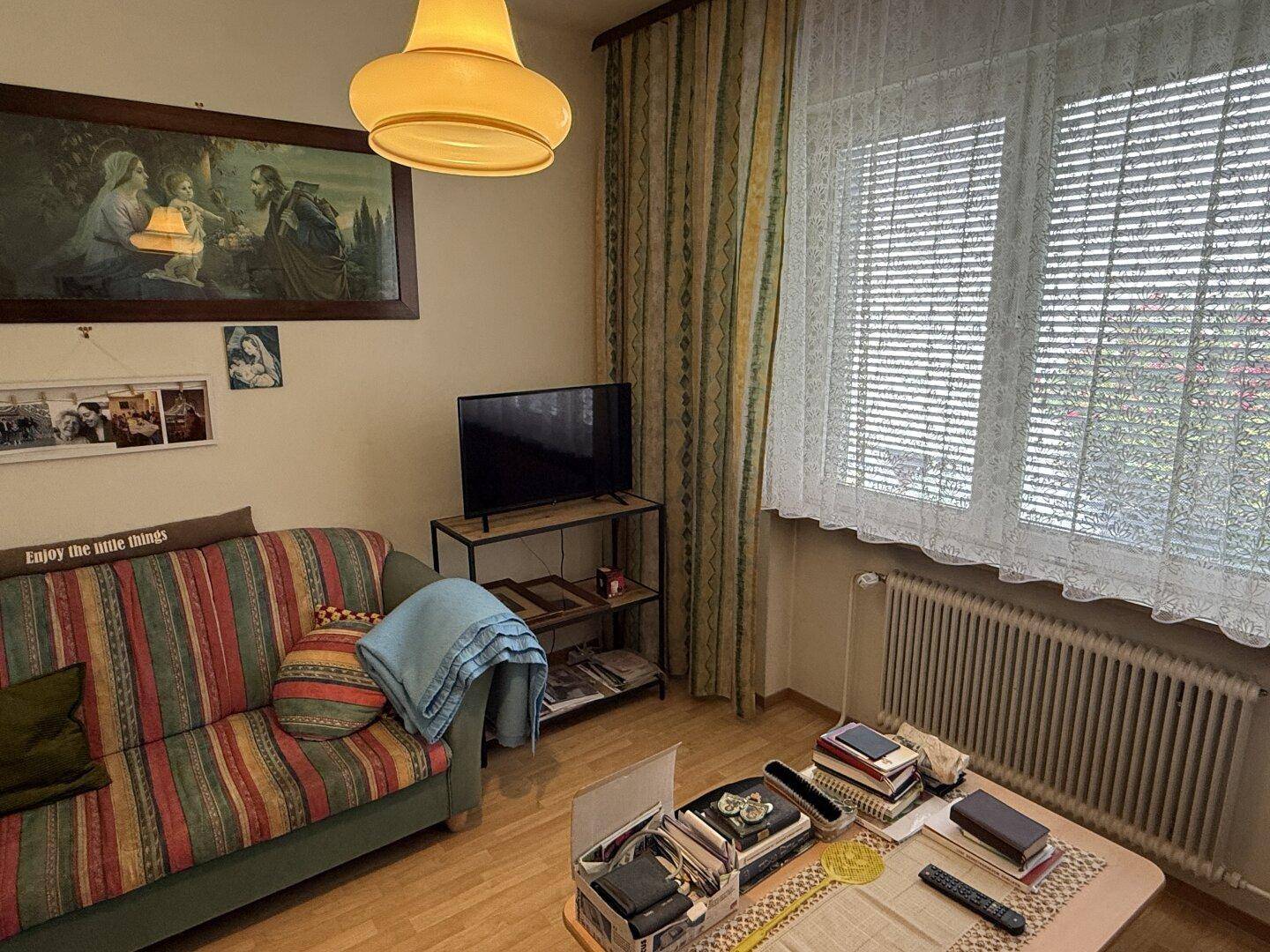 Wohnzimmer mit gestreiftem Sofa, Fernseher und hellem Fenster mit Vorhängen.