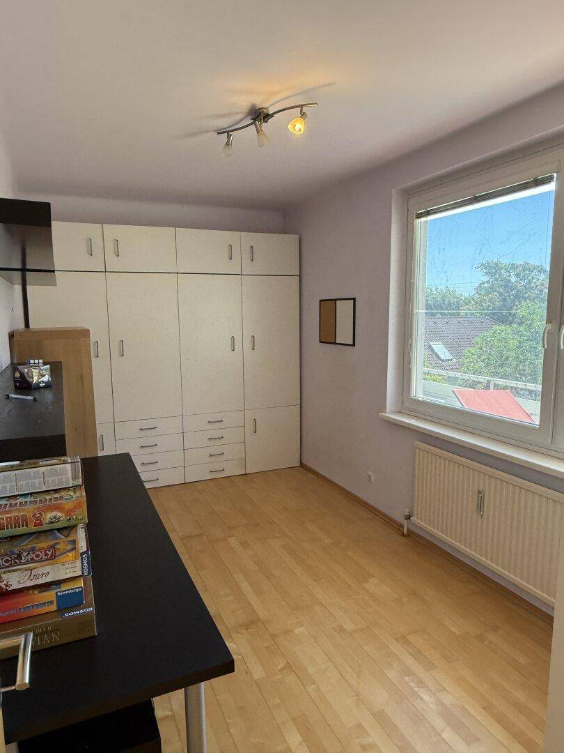 Helles Zimmer mit großem Einbauschrank, Holzboden und Fenster, das viel Tageslicht hereinlässt.