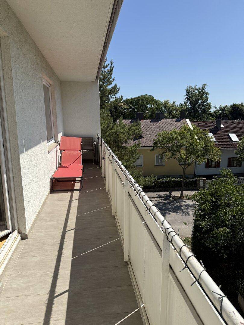 Sonniger Balkon mit Fliesenboden und Blick auf die umliegenden Häuser und viel Grün.