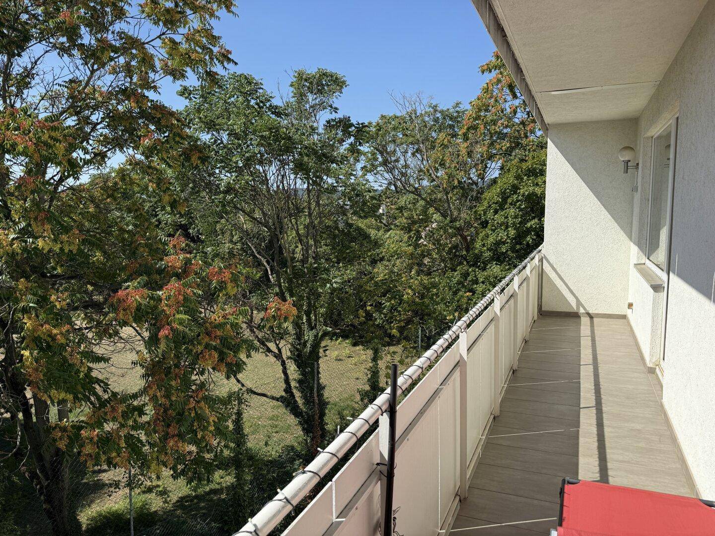 Langer Balkon mit weitem Blick ins Grüne und viel natürlichem Licht an einem sonnigen Tag.