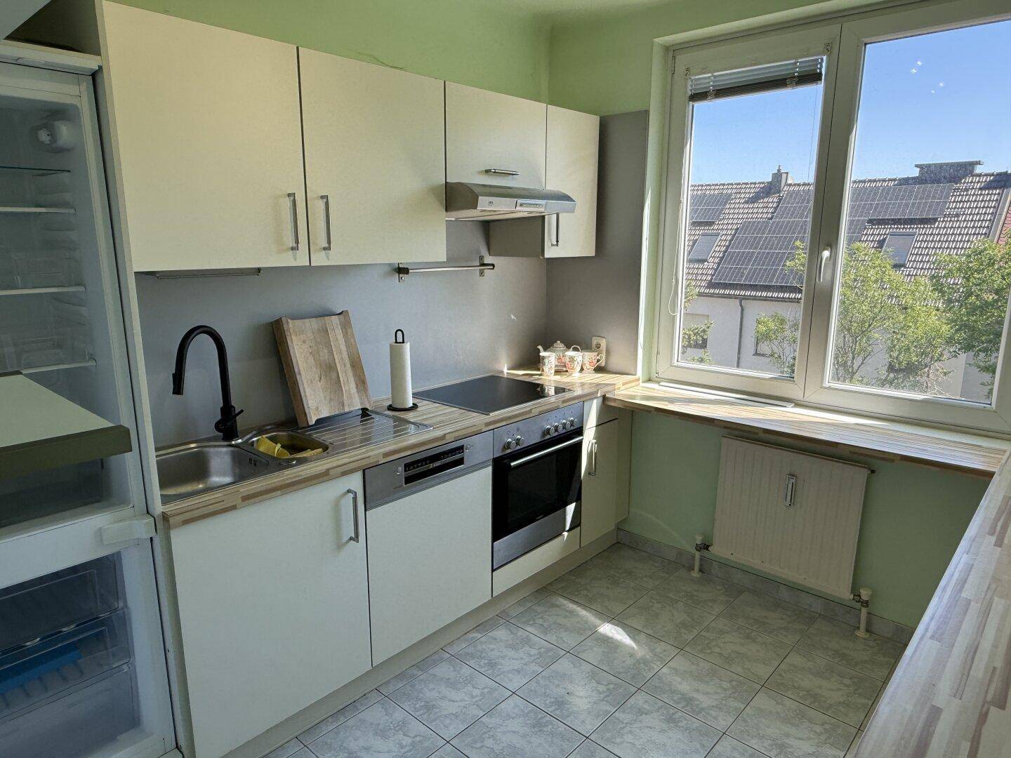 Funktionale Küche mit weißen Schränken, integrierten Geräten und einem Fenster mit Blick auf die Dächer.