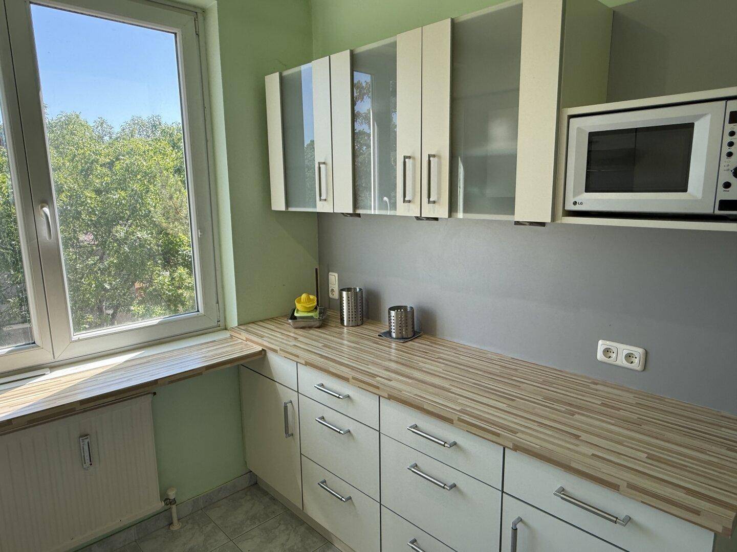 Helle Küche mit weißen Schränken, Holz-Arbeitsplatten und Mikrowelle, ideal für den täglichen Gebrauch.