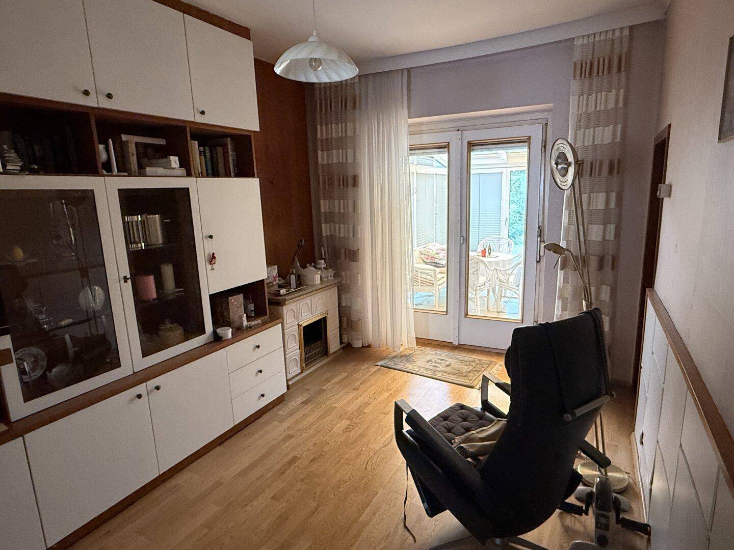 Wohnzimmer mit Holzschrankwand, Laminatboden und Zugang zu einem Wintergarten.