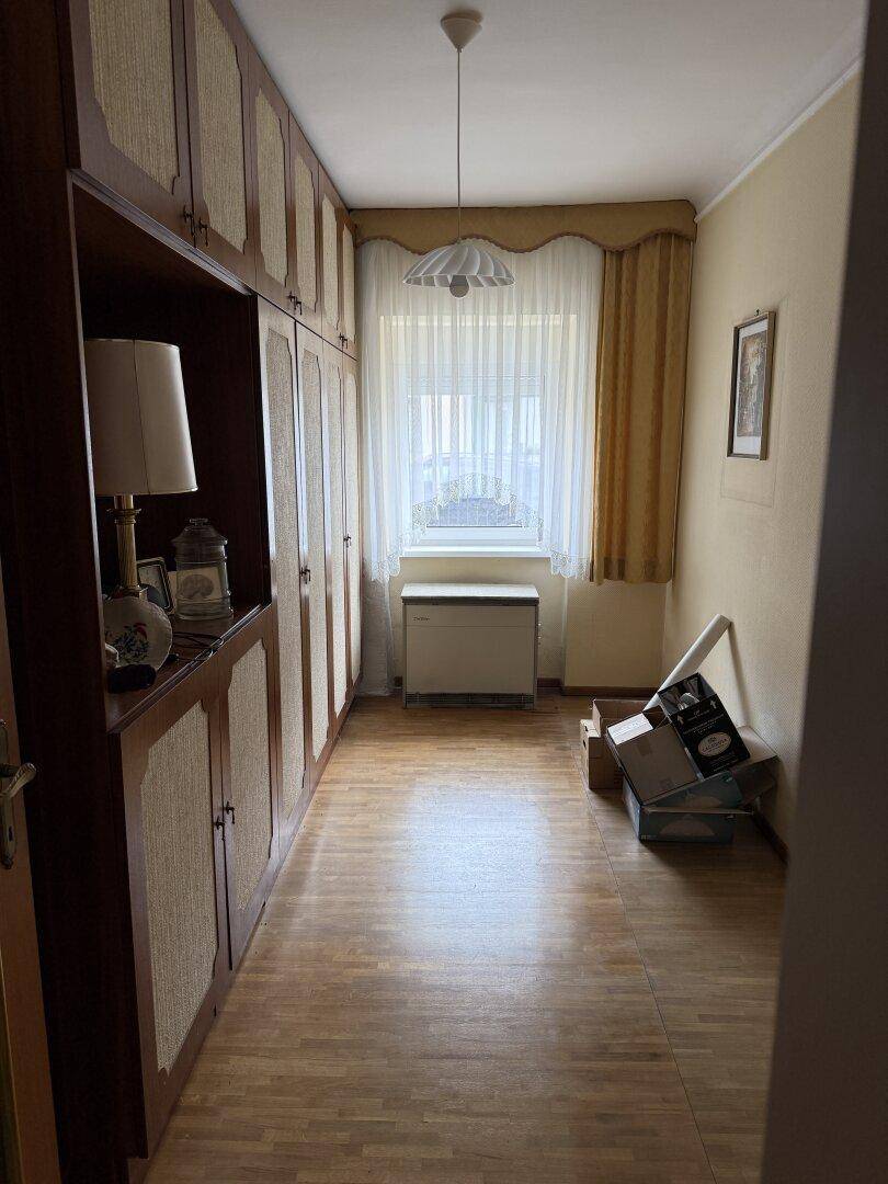 Schlafzimmer mit großem Einbauschrank, Laminatboden und Fenster mit Vorhängen.
