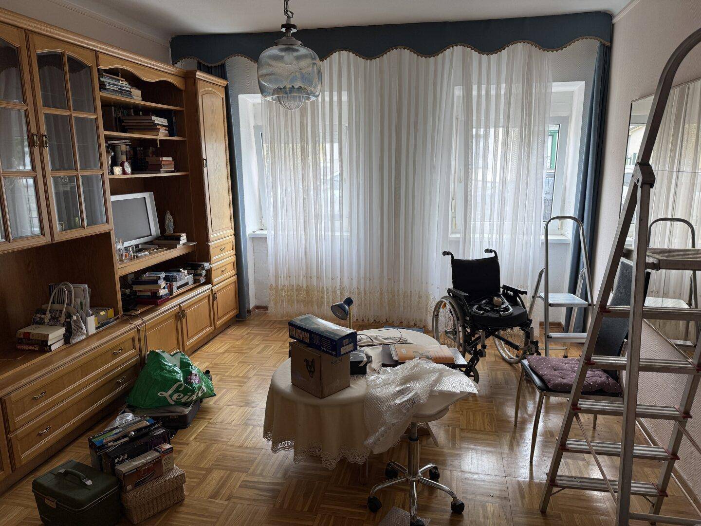 Wohnzimmer mit Holzmöbeln, Parkettboden und großen Fenstern, die viel Licht hereinlassen.