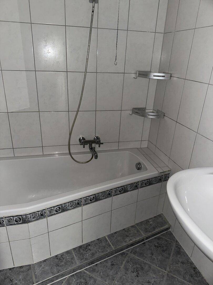 Badezimmer mit Badewanne, Duschvorrichtung und hellen Fliesen an Wänden und Boden.