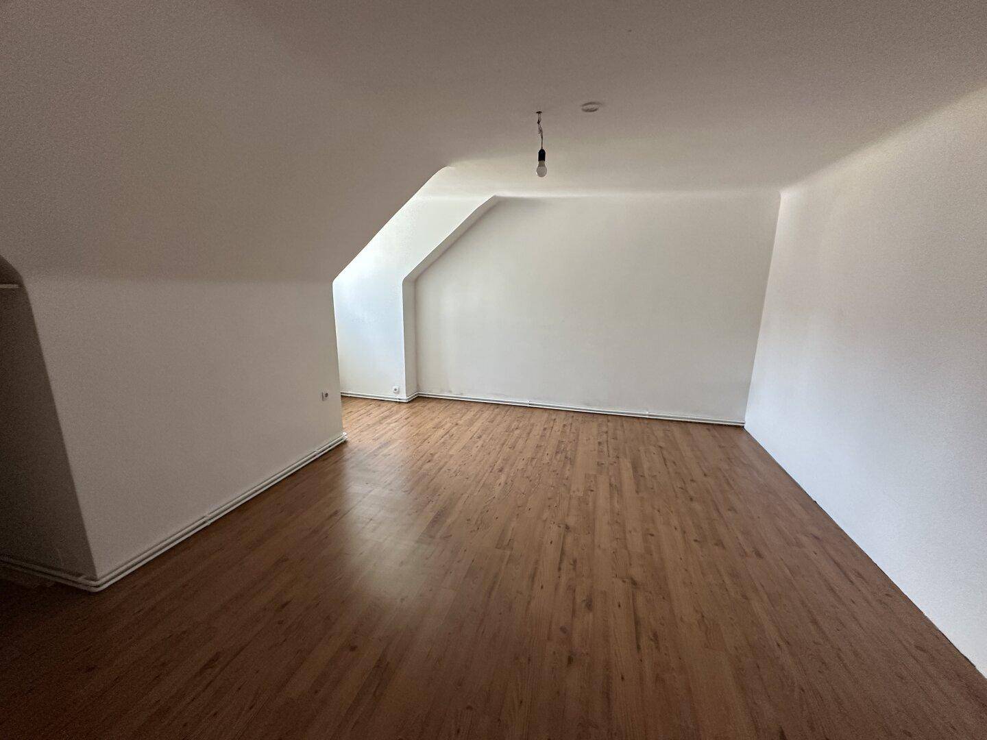 Leerer Raum mit Dachschrägen und Holzoptikboden, bereit zur individuellen Gestaltung.
