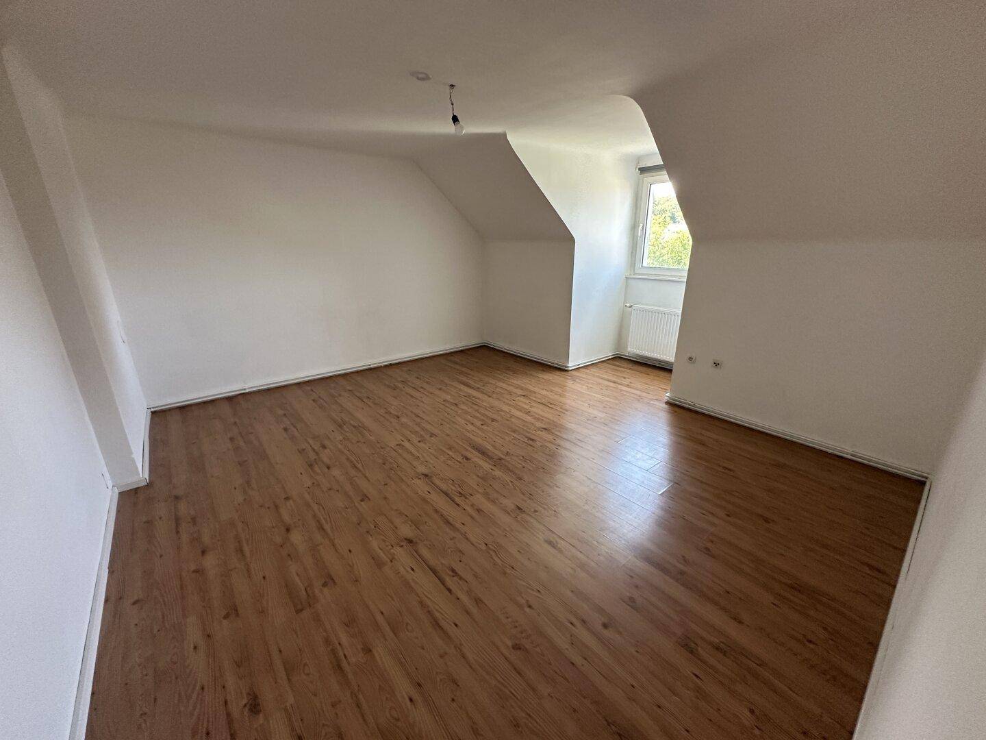 Heller Raum mit Dachschrägen, Fenster und Holzoptikboden, ideal als Schlafzimmer.