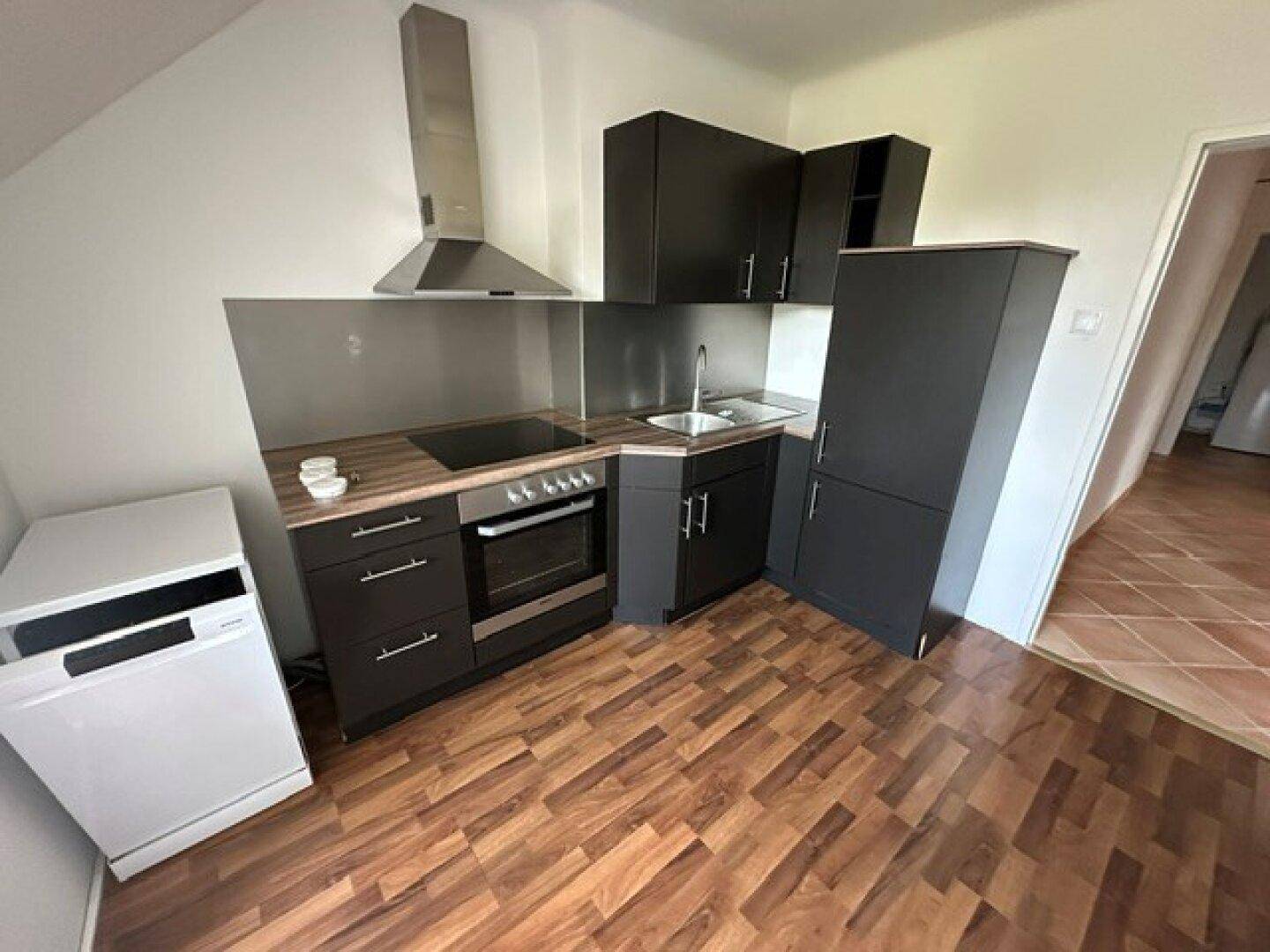 Kleine, funktionale Küche mit dunklen Schränken, integriertem Herd und Holzoptikboden.