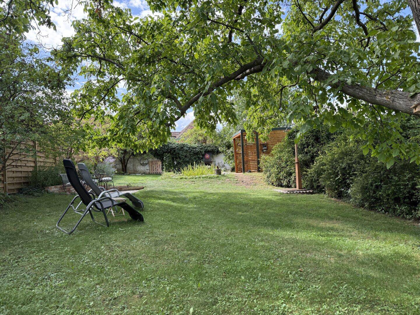 Großer, gepflegter Garten mit Rasenfläche, Liegestühlen und Blick auf die Gartensauna.