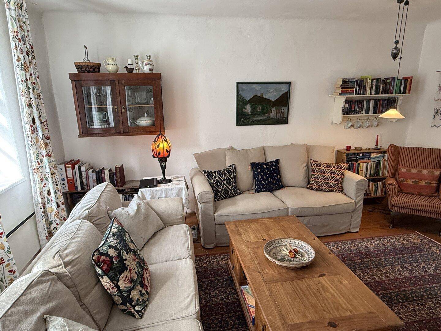 Helles Wohnzimmer mit bequemen Sofas, Bücherregalen und einem traditionellen Teppich.
