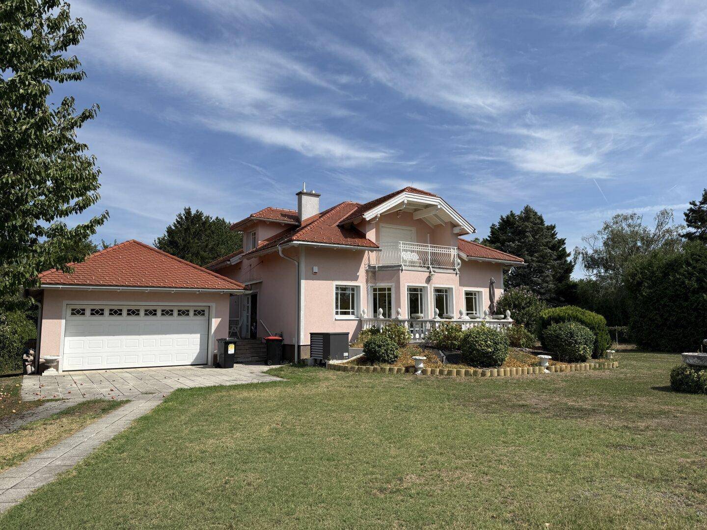 Ansicht des rosa Hauses mit Garage, gepflegtem Vorgarten und klassischer Architektur.