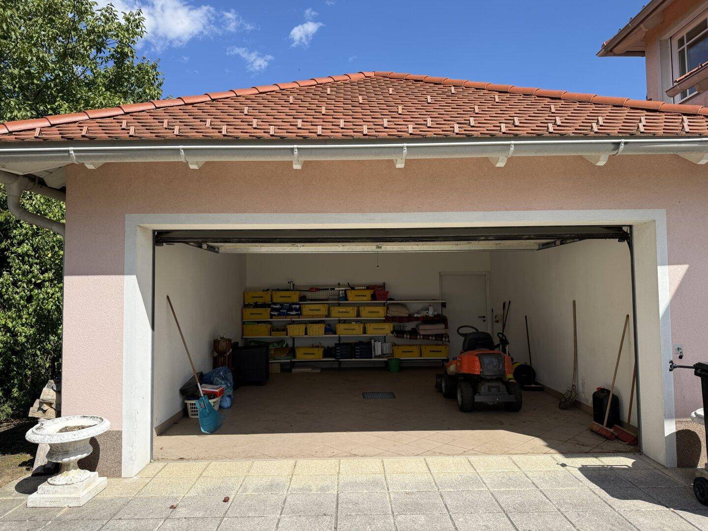 Offene Garage mit Stauraum, Werkzeugen und Gartengeräten.