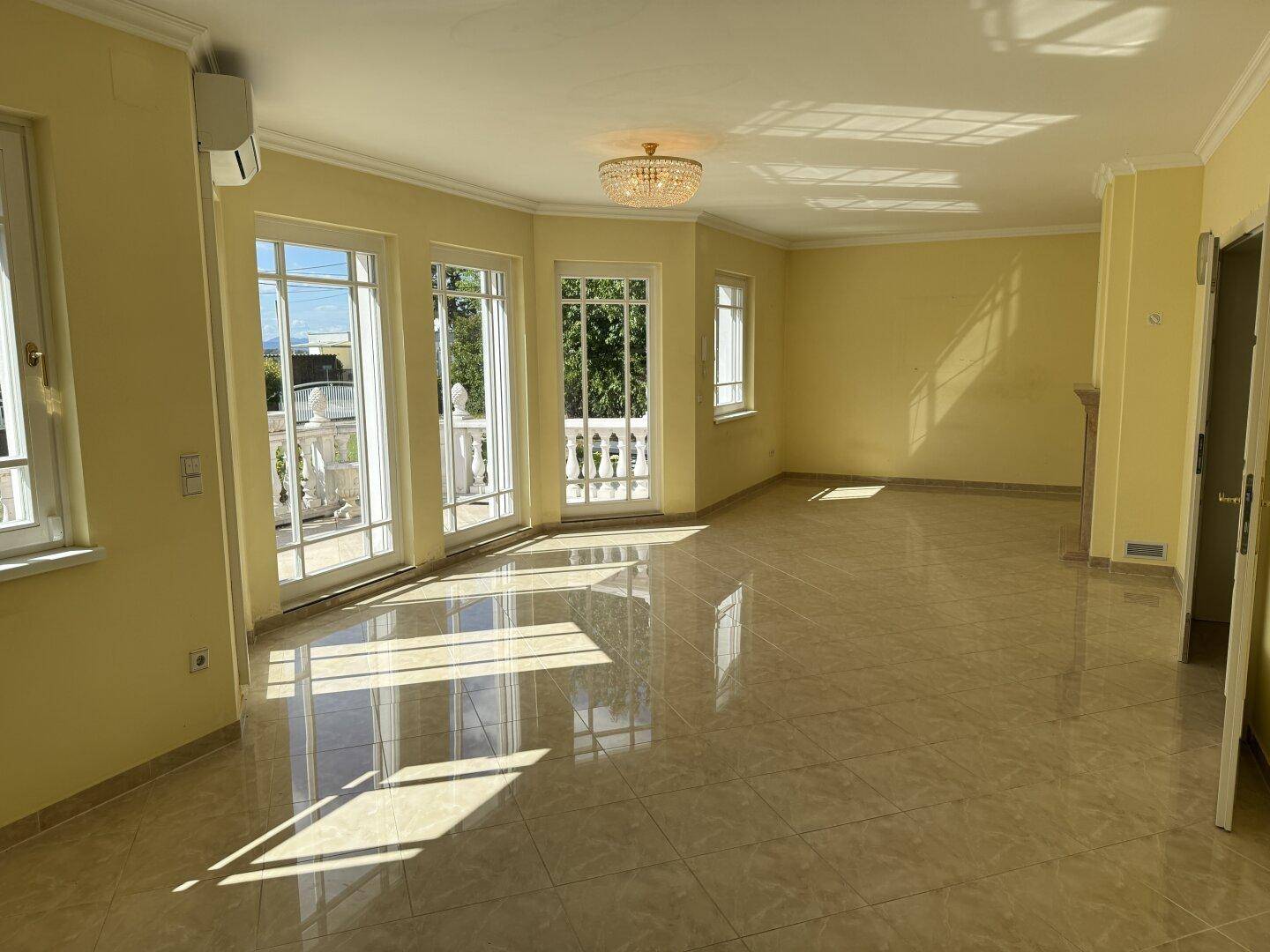 Helles Wohnzimmer mit gelben Wänden, glänzenden Fliesen und Zugang zu einem Balkon.