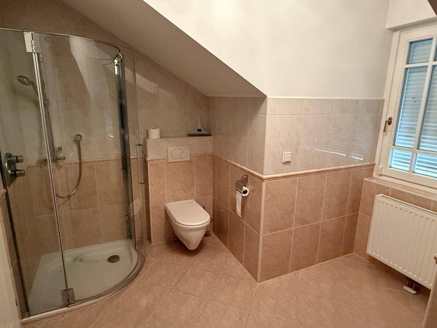 Badezimmer im Dachgeschoss mit Dusche, WC, Fenster und schrägen Wänden.