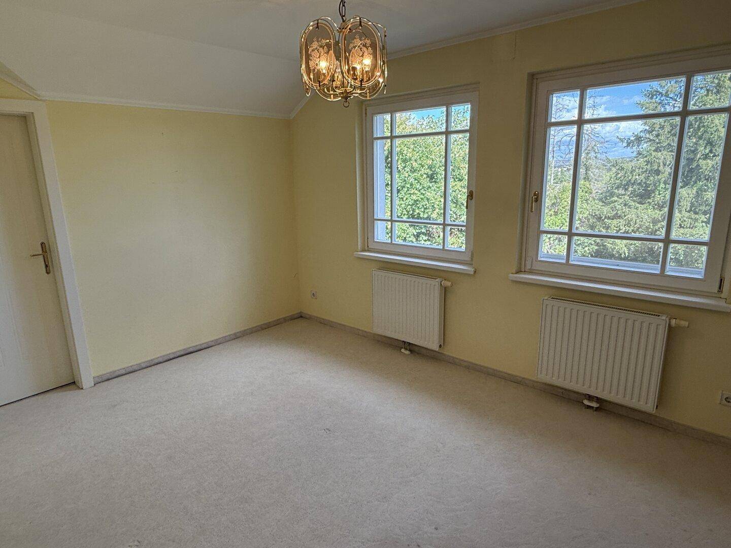 Schlafzimmer mit Teppichboden, gelben Wänden und zwei großen Fenstern.