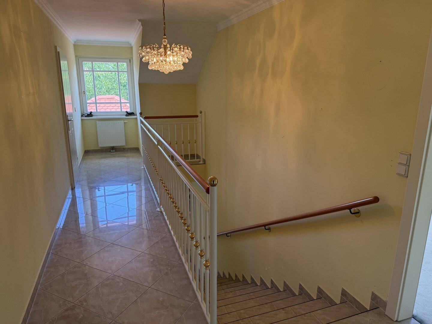 Heller Flur mit Fliesenboden und Treppe, die in die unteren Etagen führt.