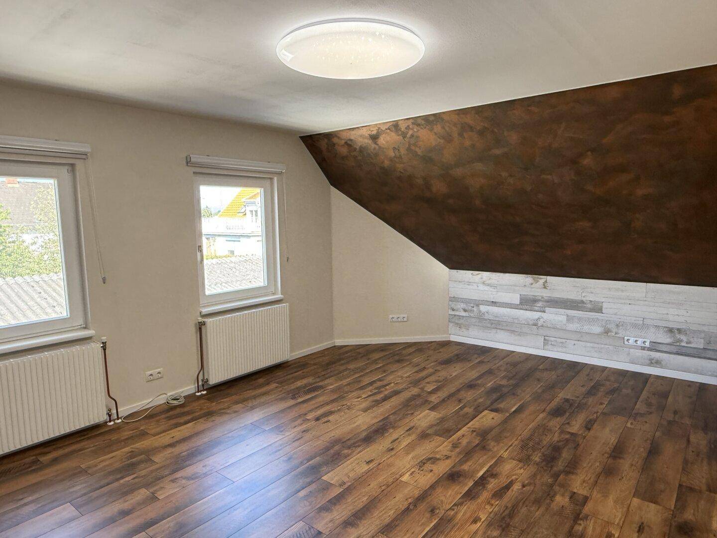 Geräumiges Schlafzimmer mit Holzboden, Dachschräge und zwei Fenstern.