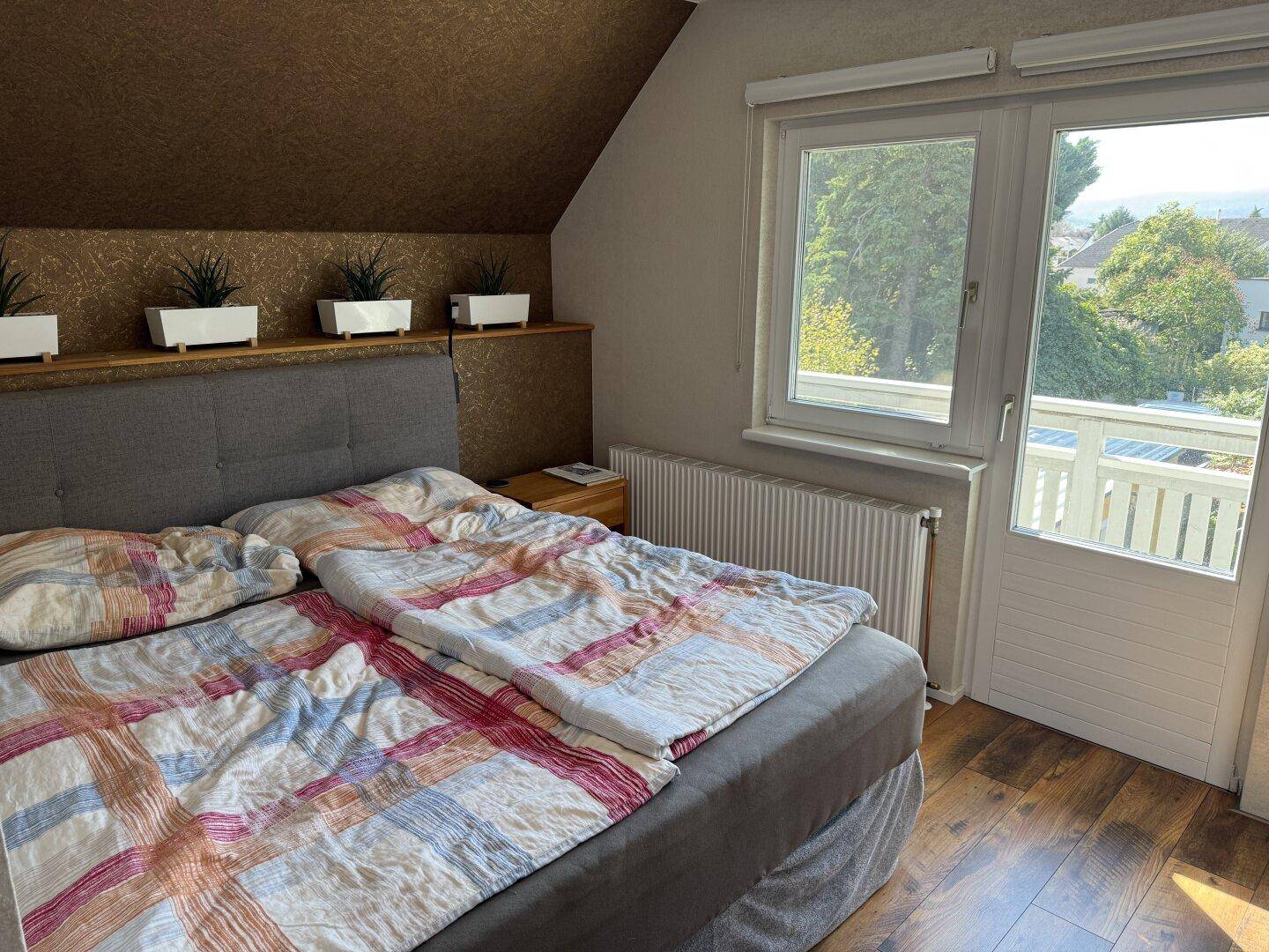 Schlafzimmer mit Doppelbett, Holzboden und Zugang zu einem Balkon mit Aussicht.