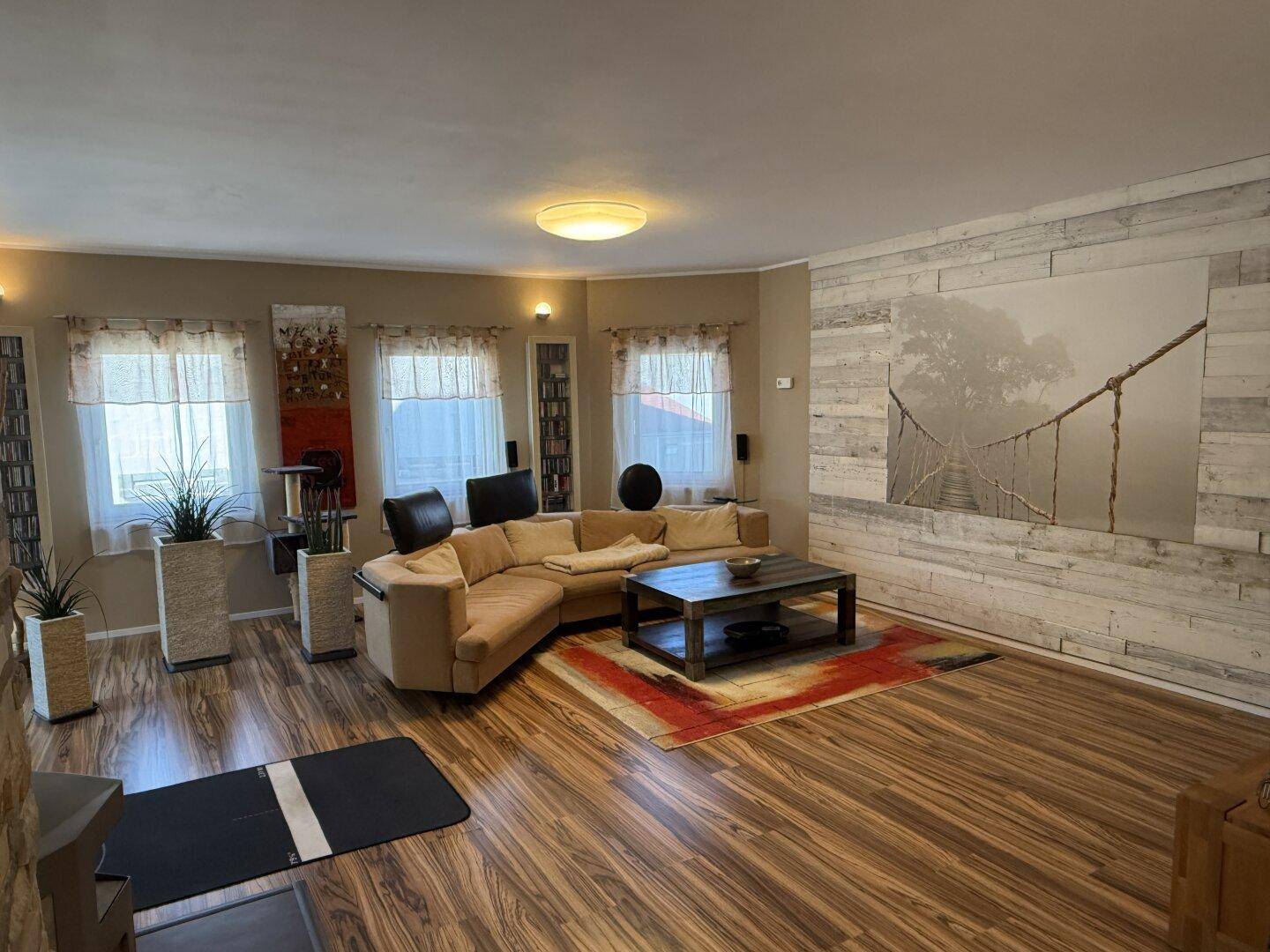Geräumiges Wohnzimmer mit beiger Eckcouch, Holzboden und dekorativer Wandverkleidung.