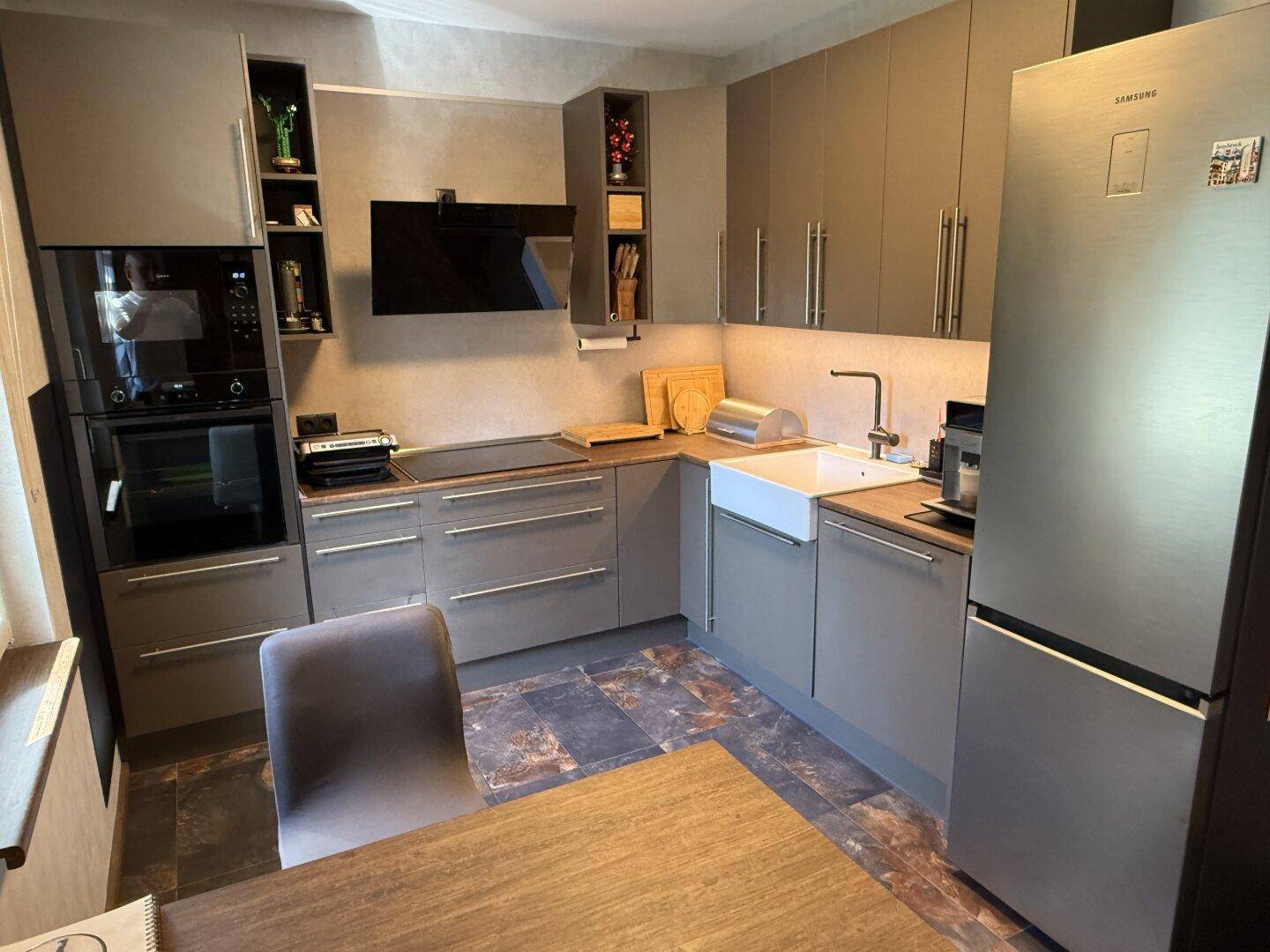Moderne Küche mit grauen Schränken, integrierten Geräten und einem großen Kühlschrank.