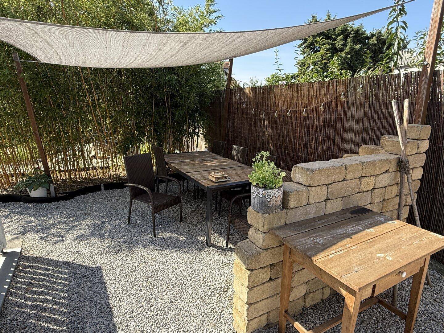 Gemütliche Terrasse mit Kiesboden, Esstisch und Sonnensegel im Gartenbereich.