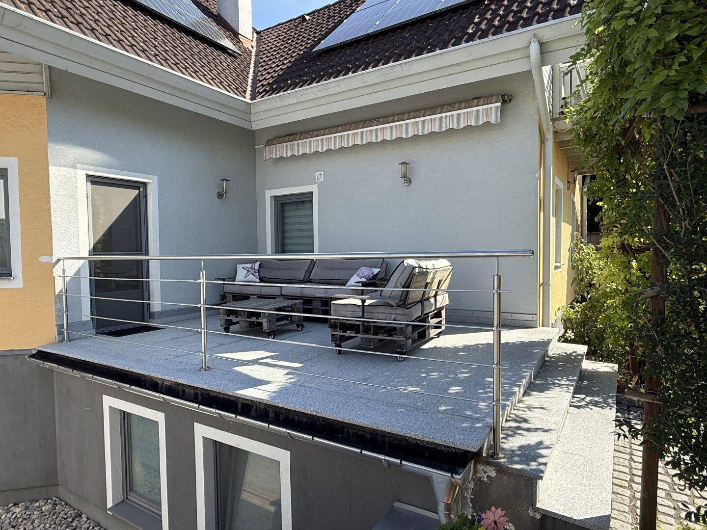 Große geflieste Terrasse mit Lounge-Möbeln und Edelstahlgeländer.