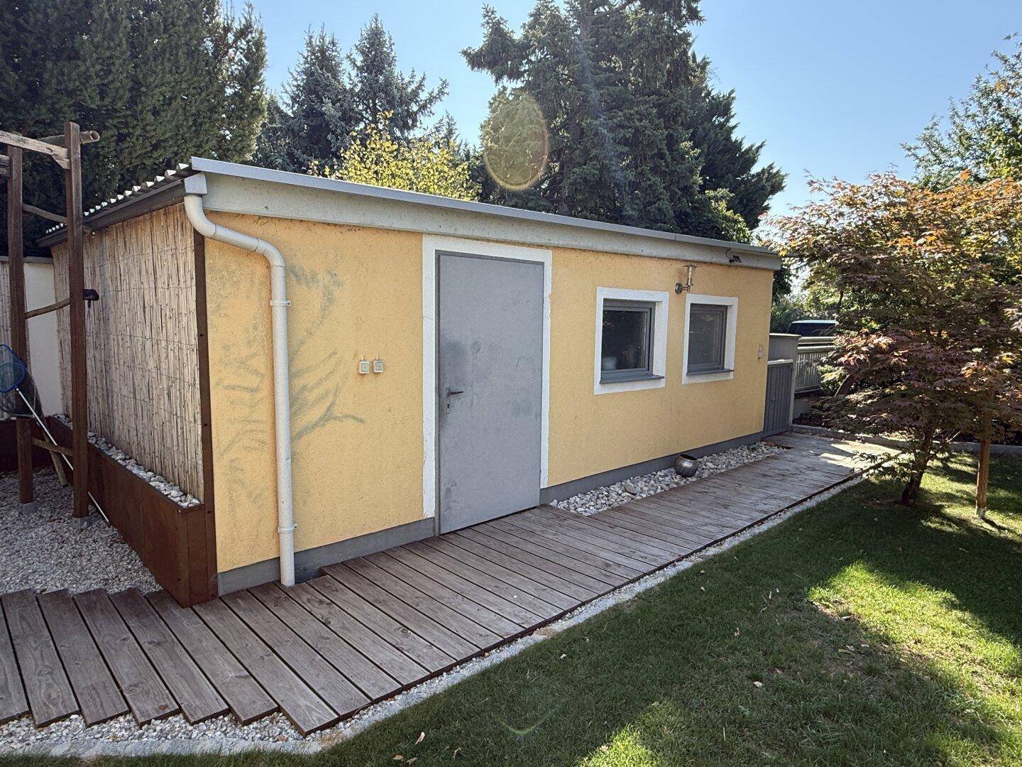 Gelbes Nebengebäude mit Holzdielenweg und umgebender Grünfläche.